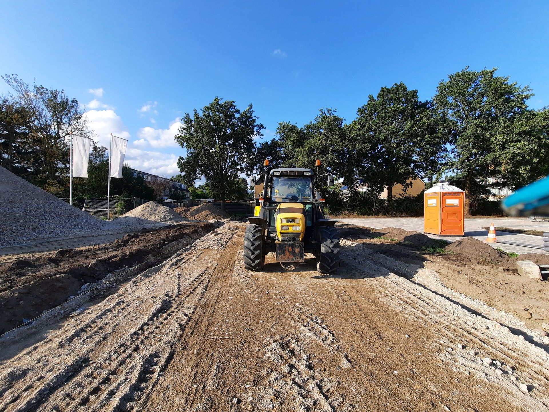 A tractor on a construction site with dirt road and trees under blue sky.